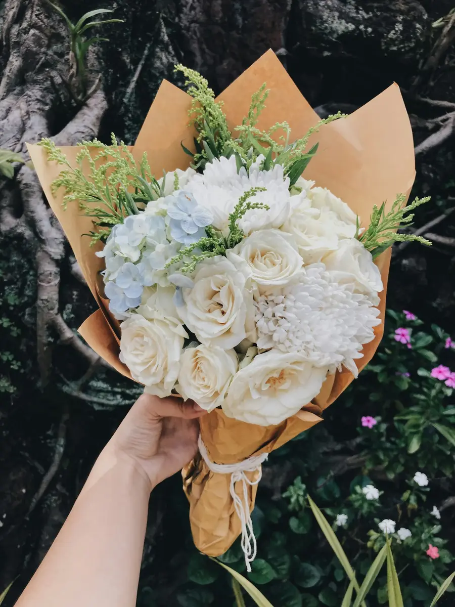 Wit boeket met rozen en hortensia in bruin papier, vastgehouden in de hand