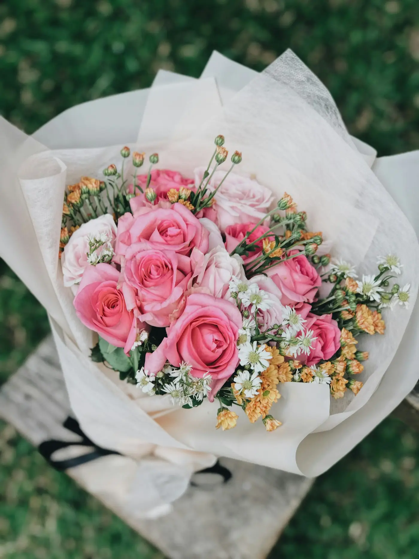 Boeket met roze en witte rozen in wit papier, gezien van boven op het gras