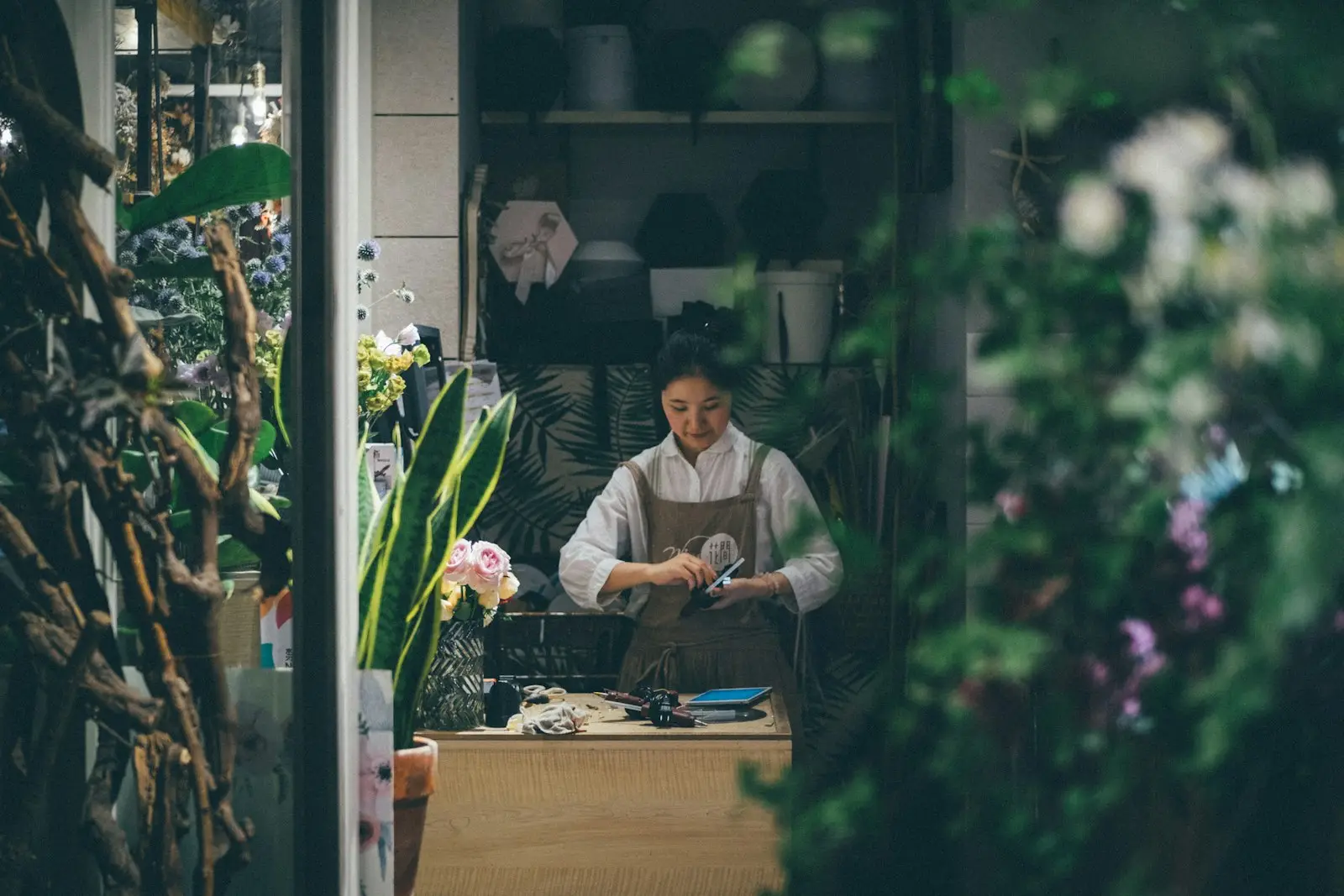 Bloemiste achter de werkbank in de winkel, tussen planten en boeketten